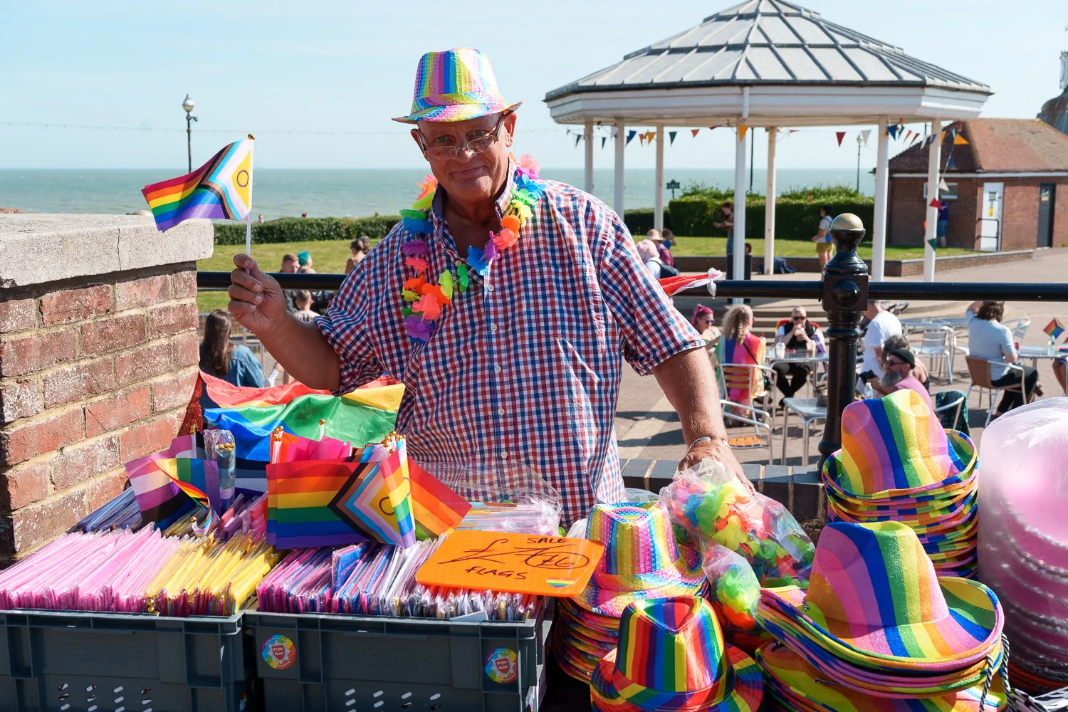 A stallholder surrounded by rainbow hats, flags and decorations