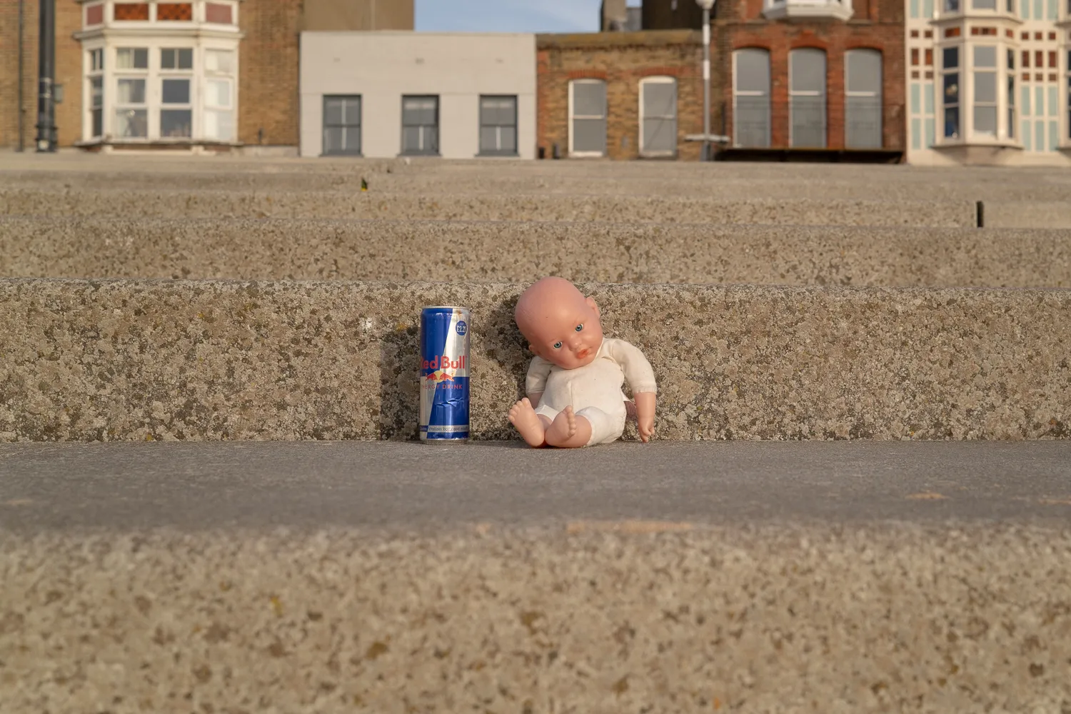 A baby doll and a drinks can propped against a wall on the seafront