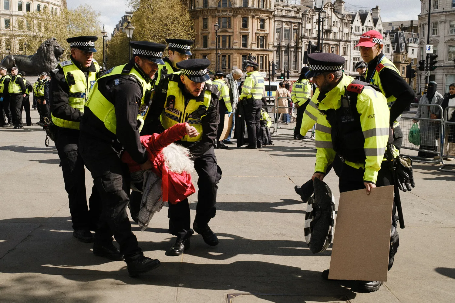 Police officers carrying a woman dressed in red with her fist forward