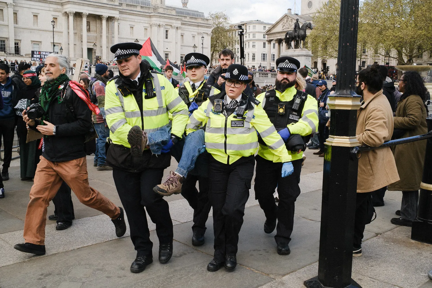 A group of police officers moving with a detainee through Trafalgar Square