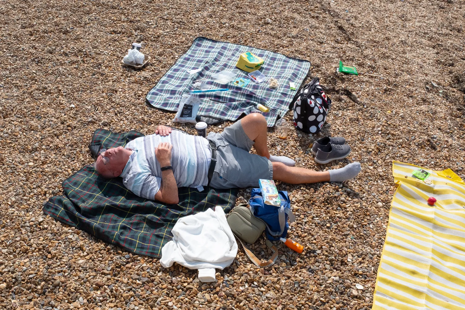 A person resting on a blanket on a shingle beach