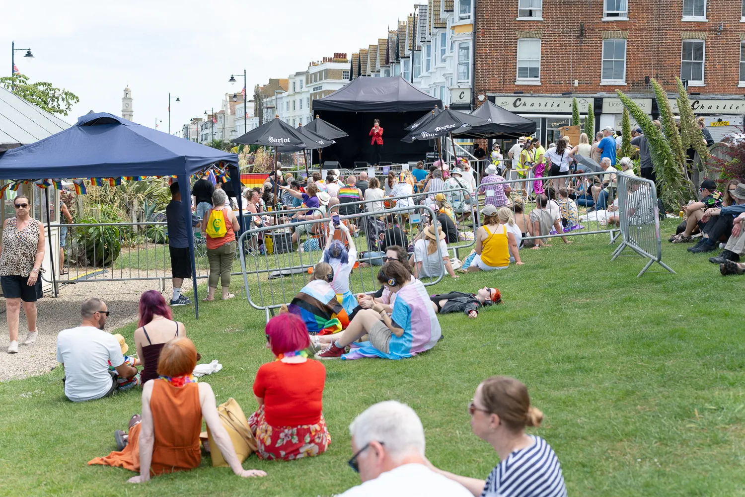 People relaxing on grass at a Pride event beside seafront houses